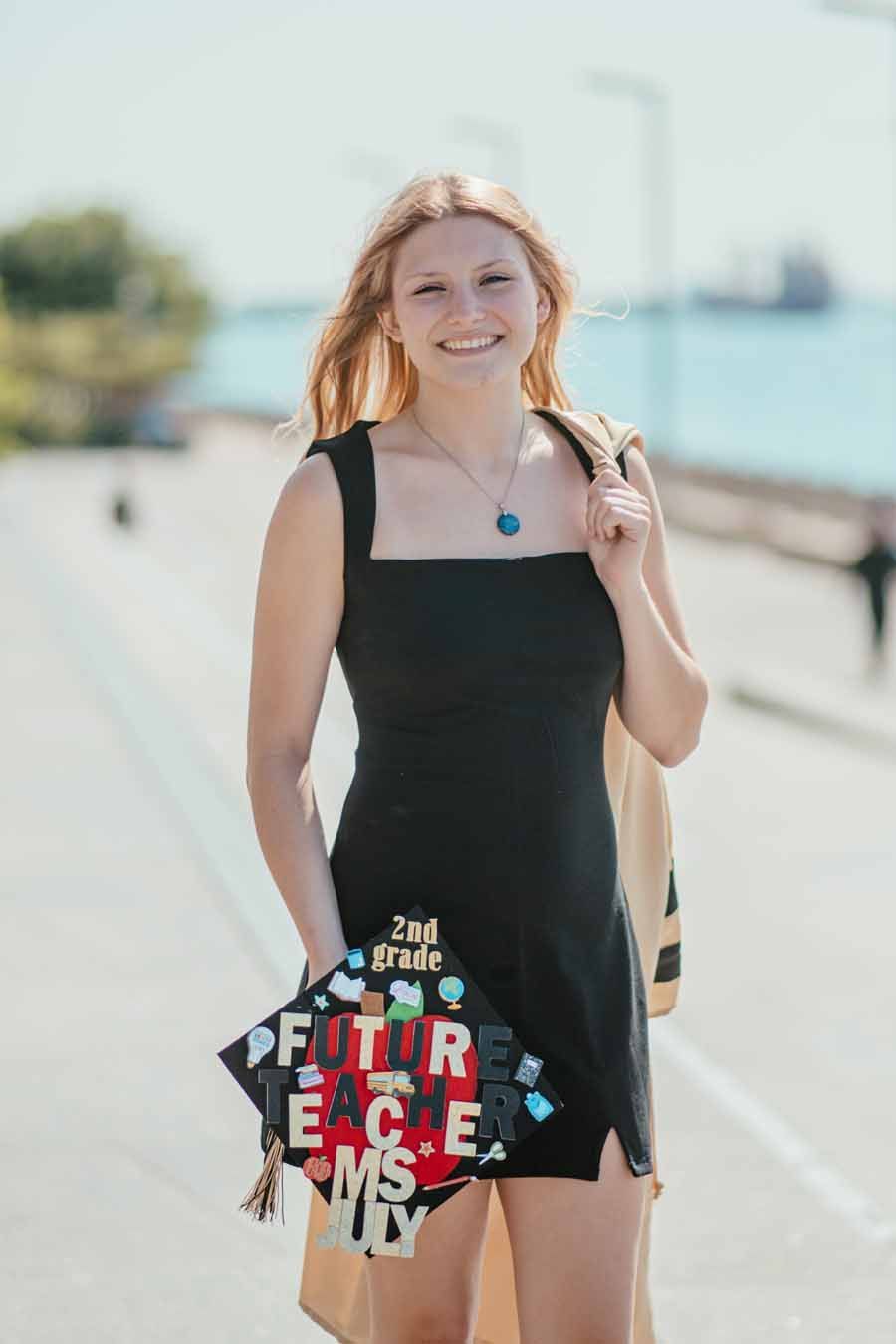 Woman in a black dress holding a colorful “Future Peace” sign on a sunny waterfront path.
