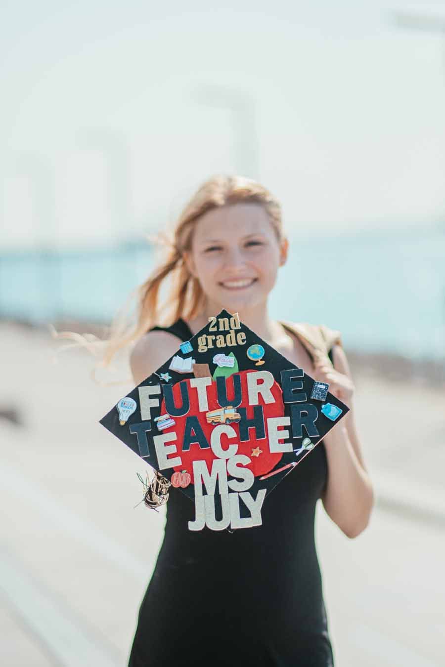 Person holding a colorful sign outdoors on a bright day, smiling in a black T-shirt.