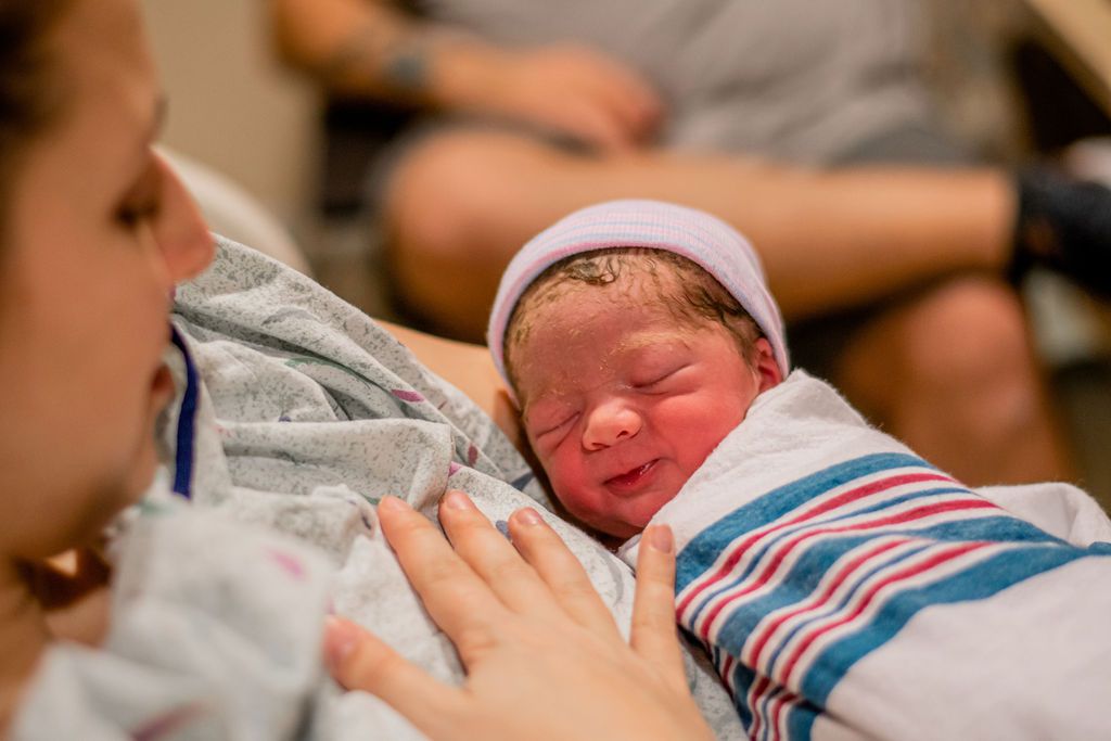 Newborn baby wrapped in a striped blanket, held close by an adult in a hospital setting
