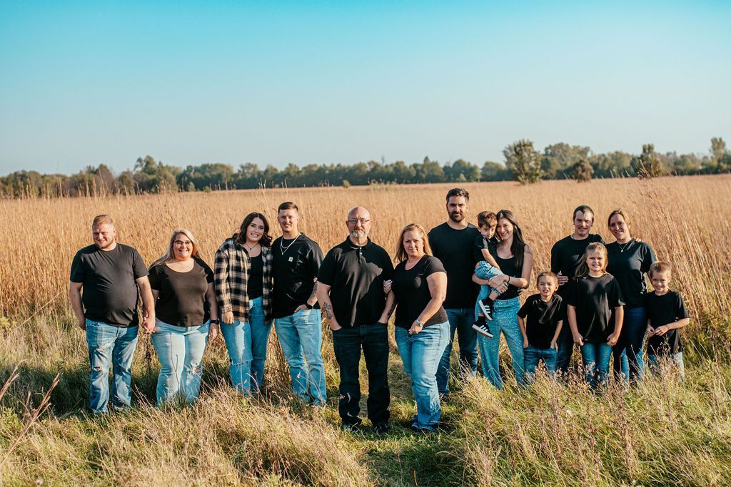 Group of people standing in a grassy field with tall dry reeds under a blue sky