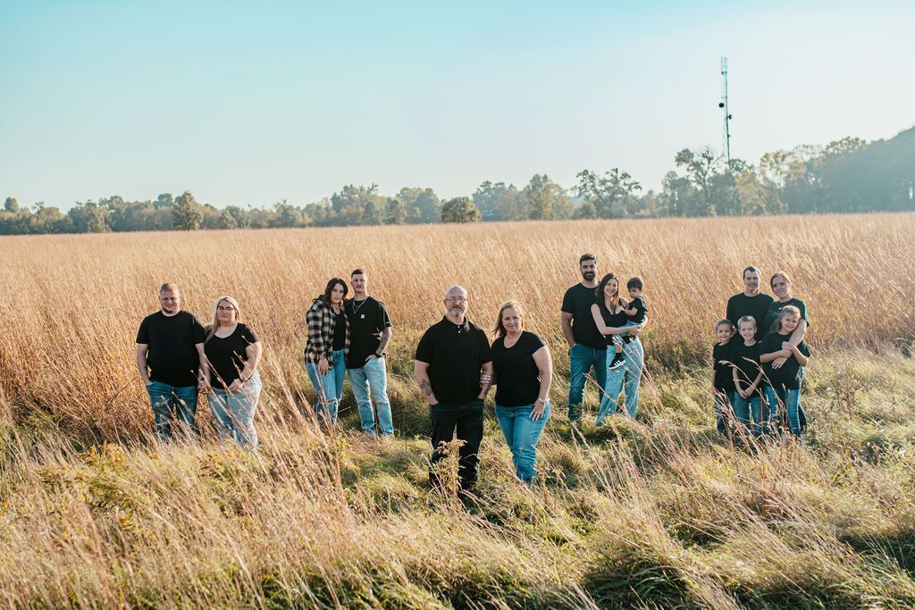 Group of people standing in a grassy field beside tall golden crops under a clear sky