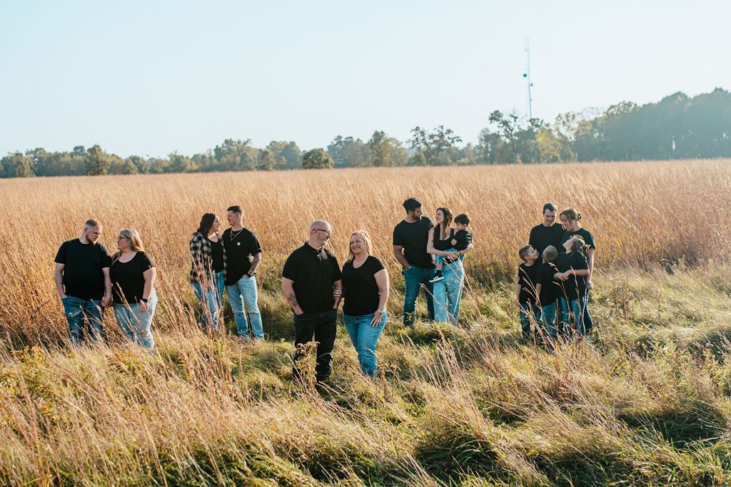 Group of people walking through tall dry grass in a sunny field with trees in the distance