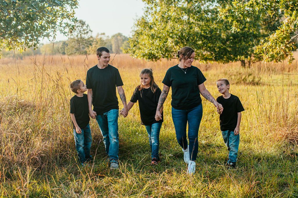 Five people walking through a grassy field with tall golden grass and trees in the background.