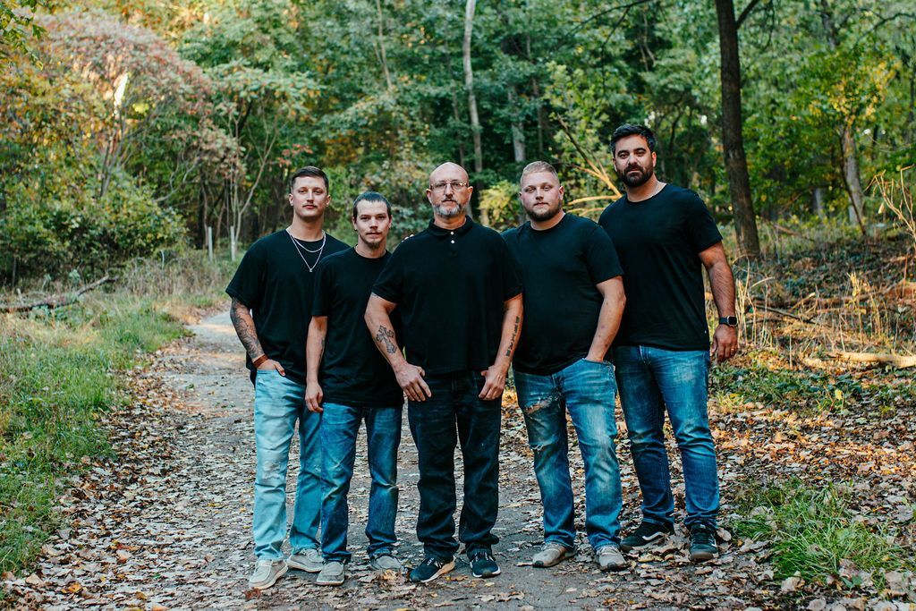Five people in black shirts and jeans standing on a wooded trail