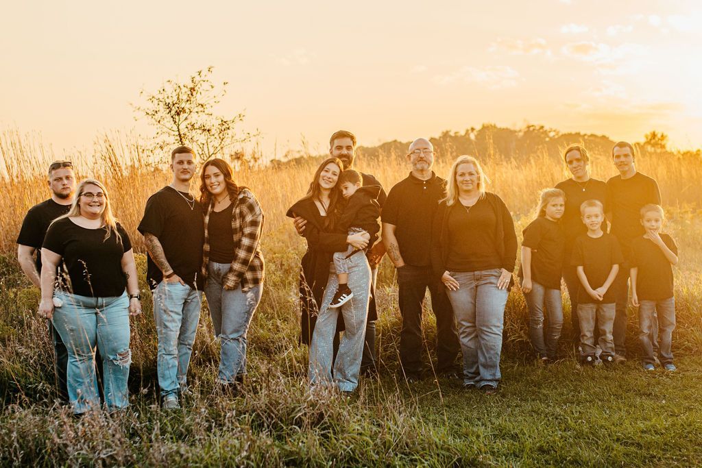 Group of people standing in a grassy field at sunset, smiling toward the camera.