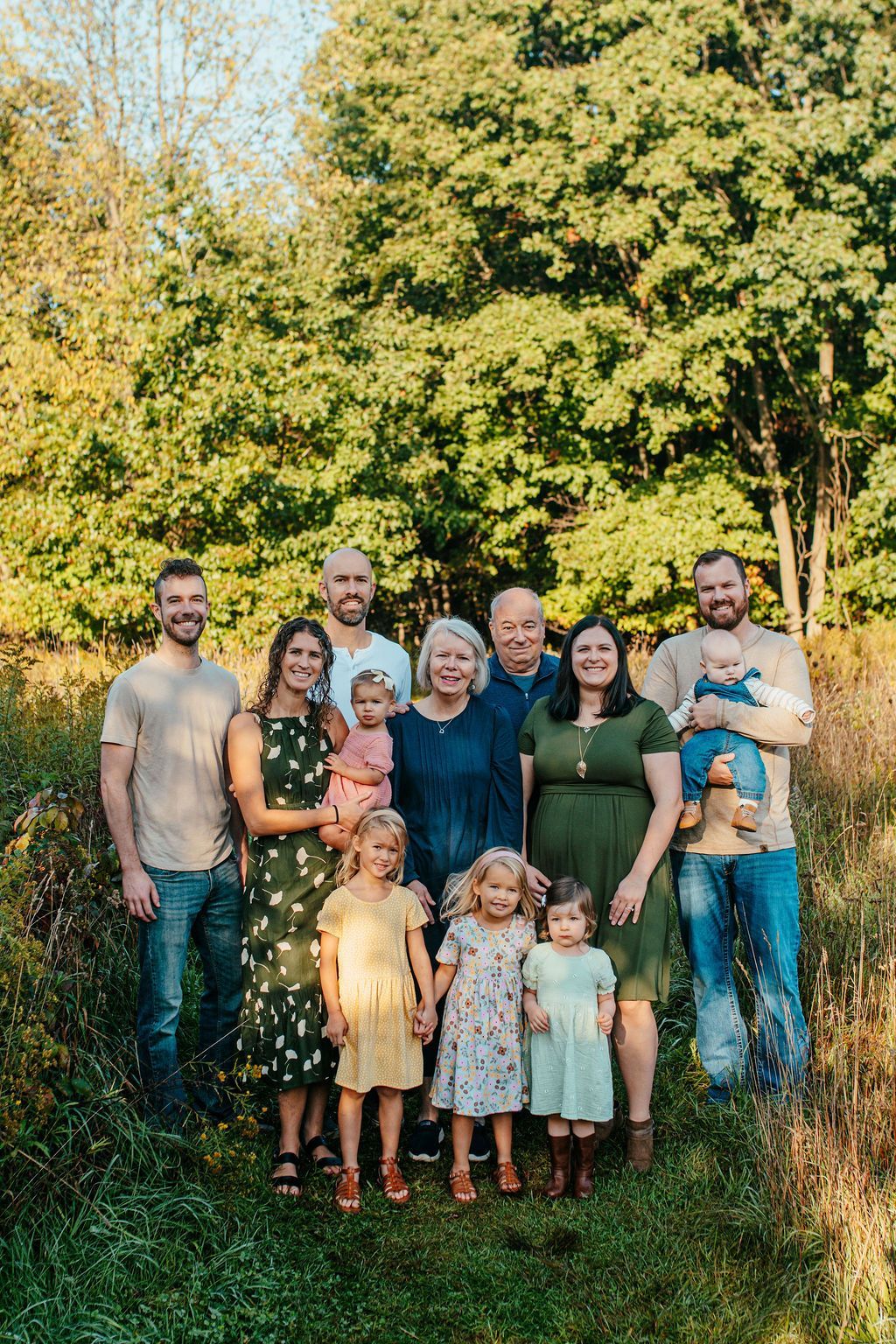 Large family standing together outdoors in a grassy field with trees in the background