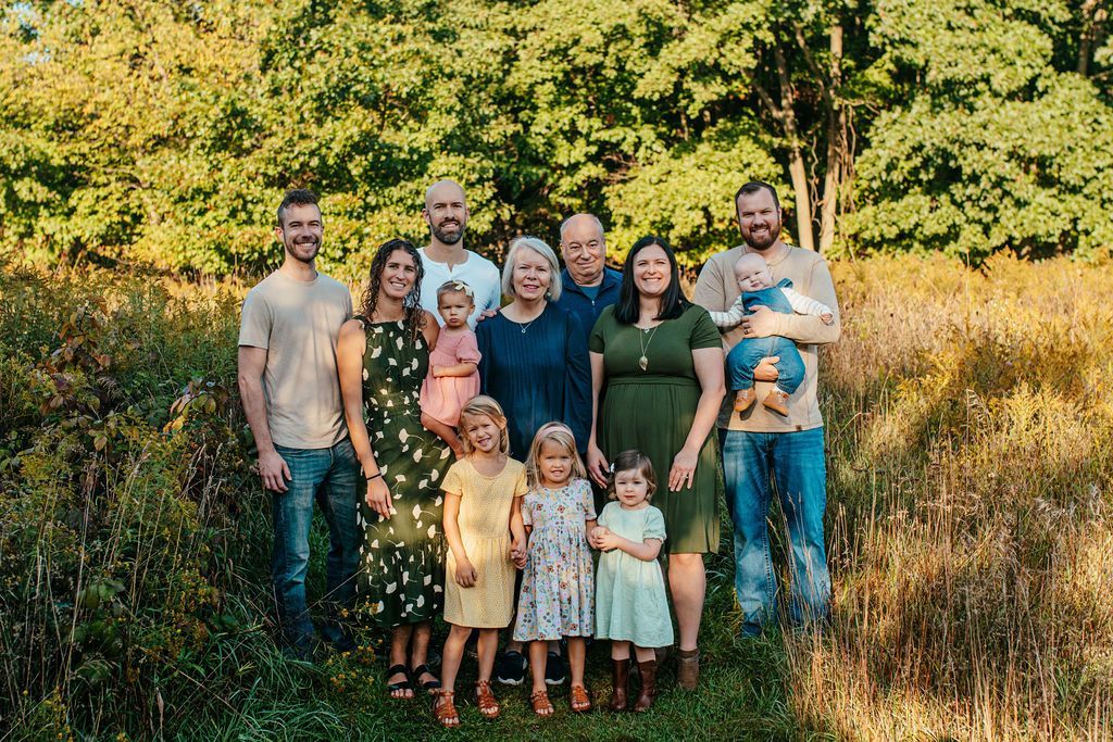Large family group posing together in a grassy field with trees in the background.