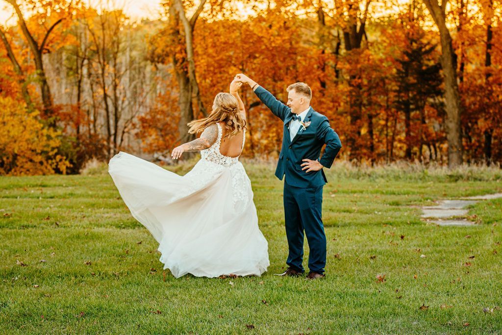 Couple dancing on a grassy field, with autumn trees glowing orange in the background.