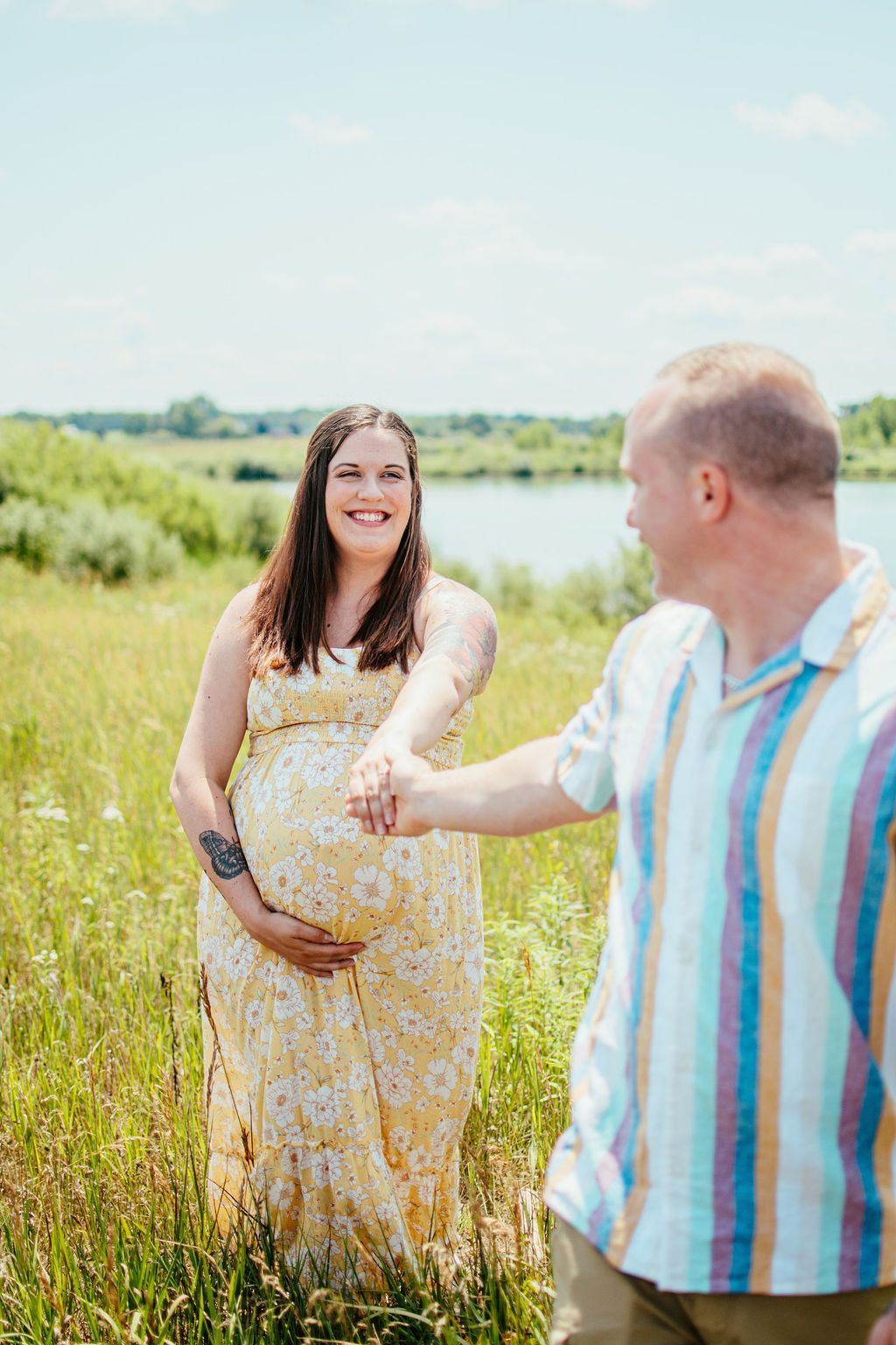 Pregnant woman in a yellow dress smiling at a man in a striped shirt in a grassy field