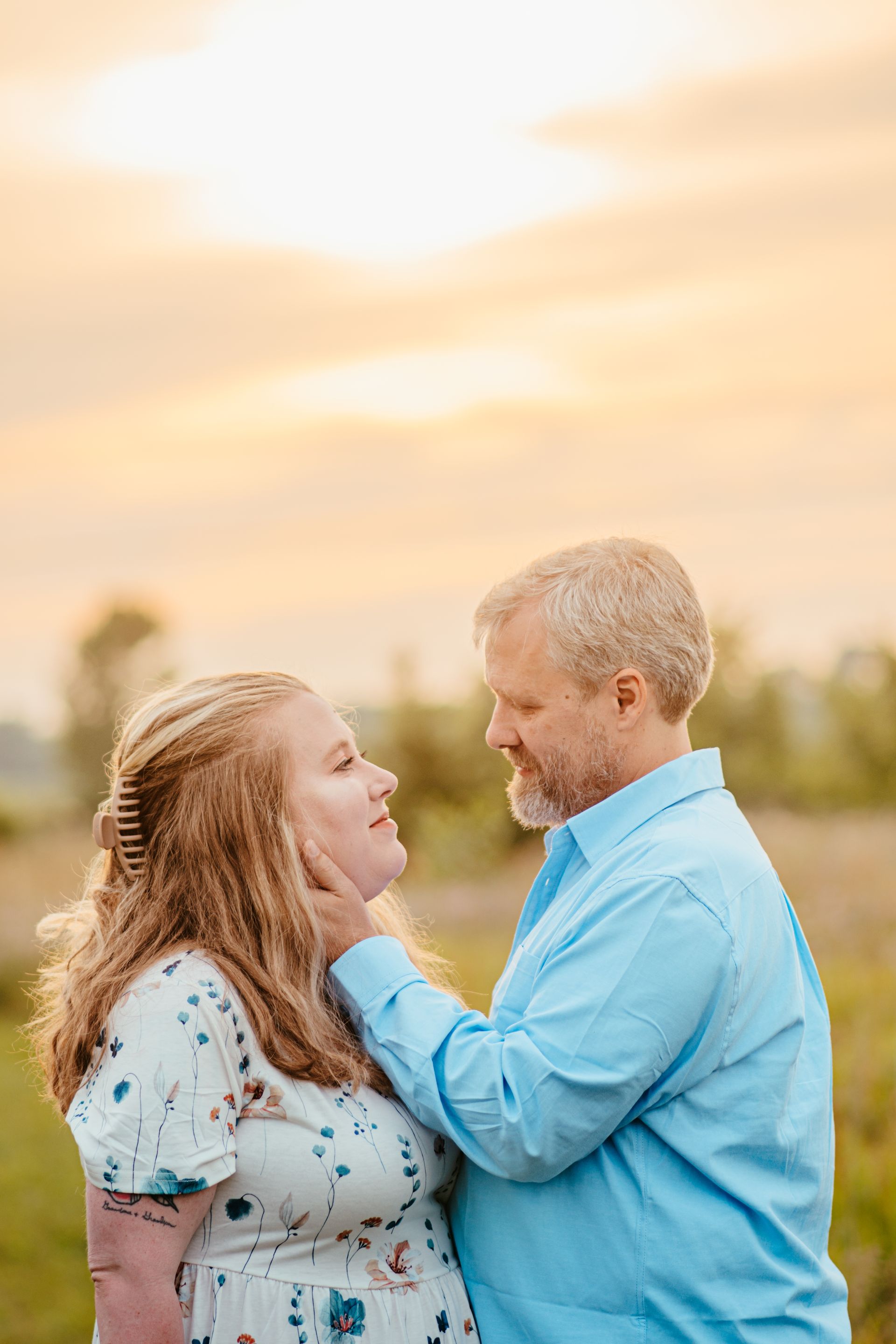Two people smiling and facing each other outdoors at sunset, with one holding the other's shoulders.