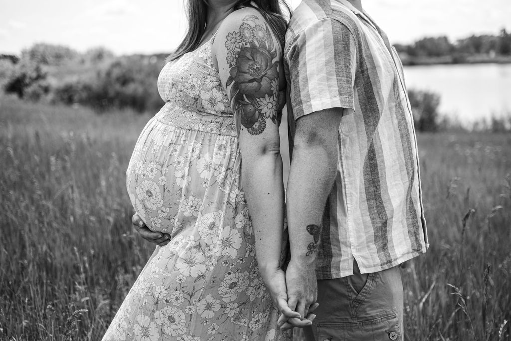 Pregnant couple holding hands in a grassy field, standing close together outdoors.