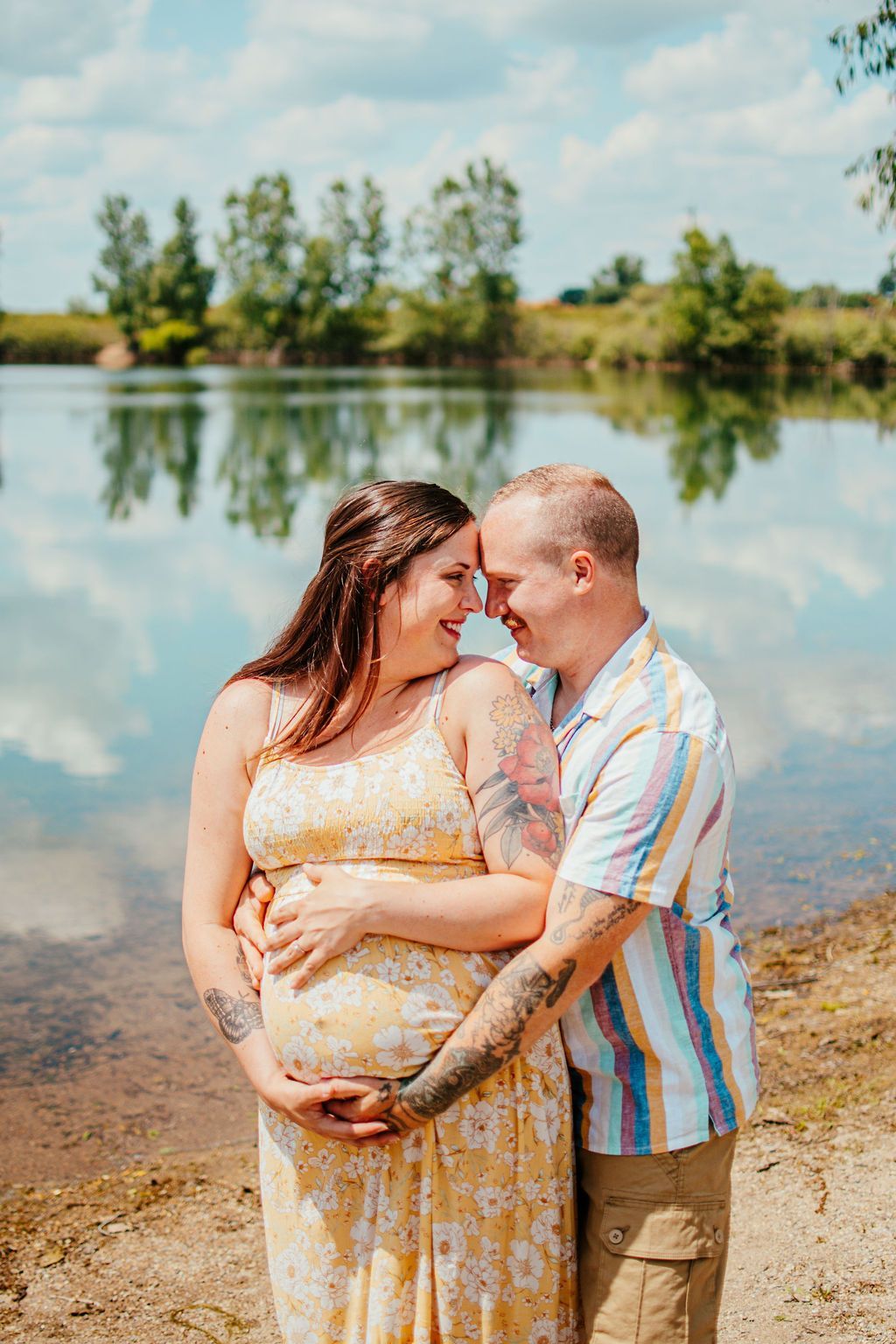 Couple embracing by a lakeside, smiling in a sunny outdoor setting