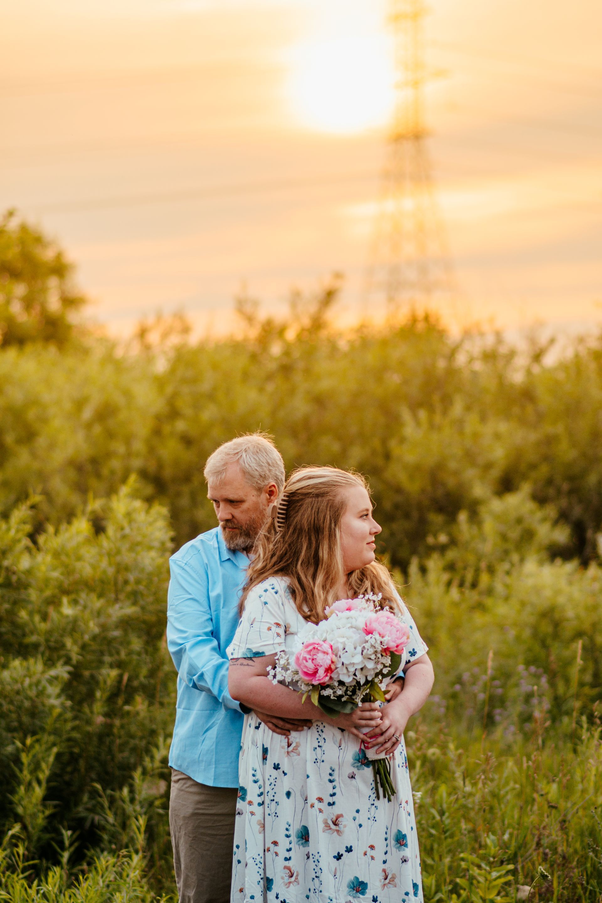 Man and girl holding a bouquet in a grassy field at sunset