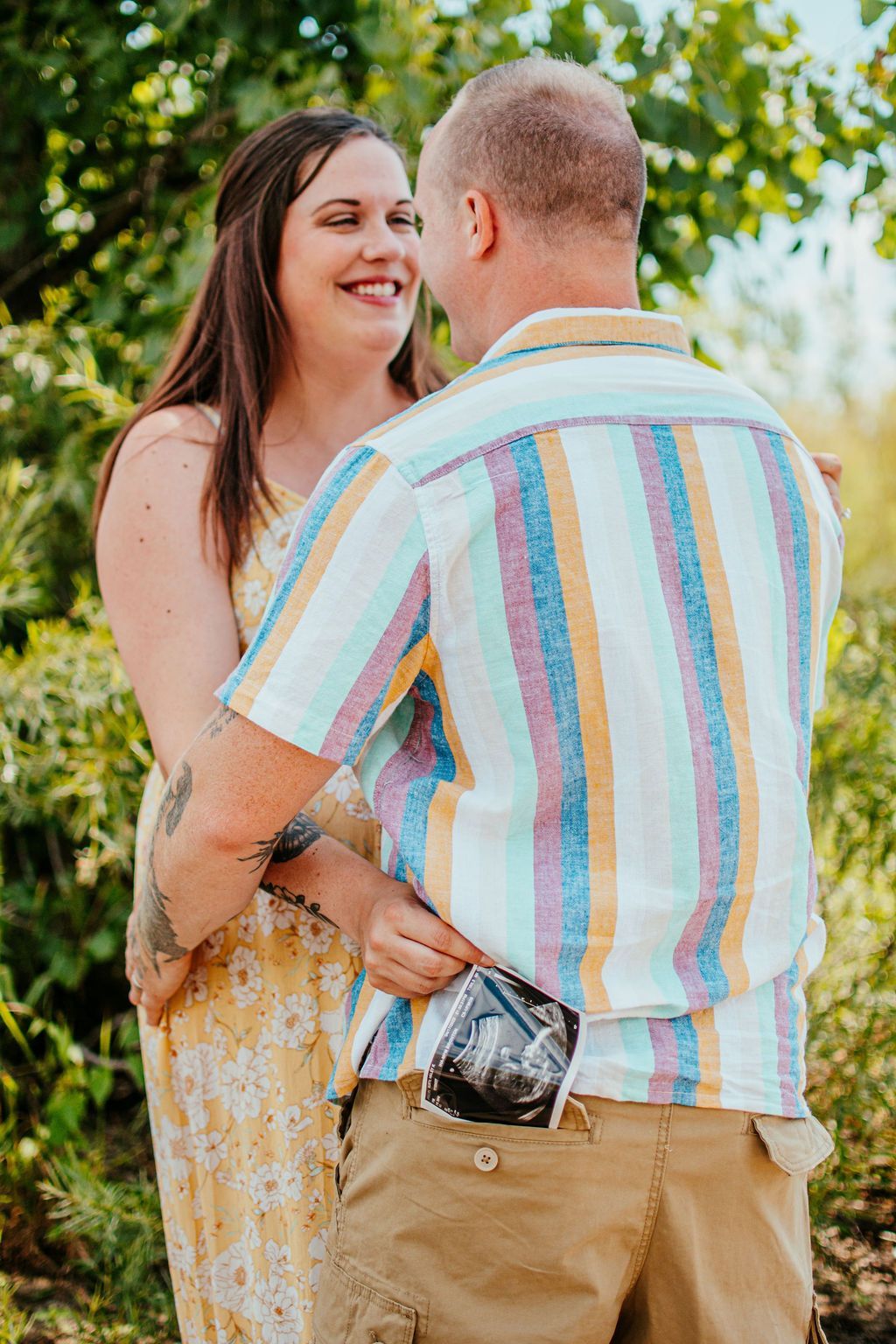 Couple embracing outdoors, smiling in a pastel-striped shirt and yellow dress
