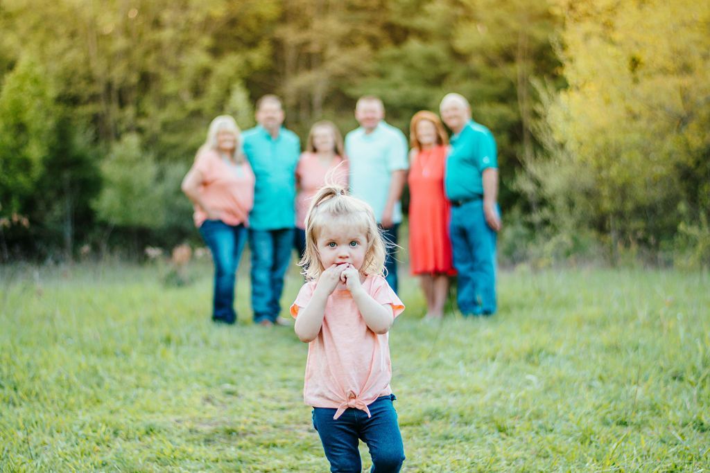 Young child standing in a grassy field with adults blurred in the background