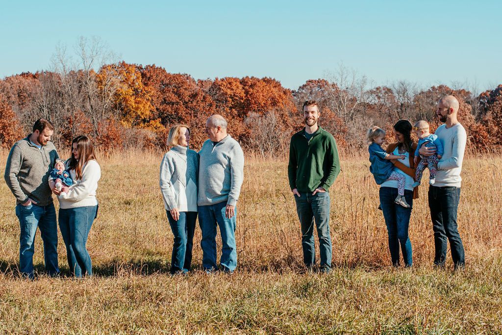 Group of people standing in a grassy field with autumn trees in the background