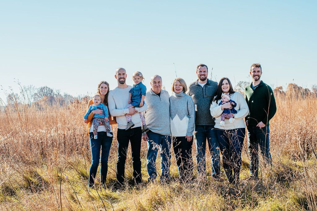 Eight people standing in a sunlit field of tall dry grass with trees in the background