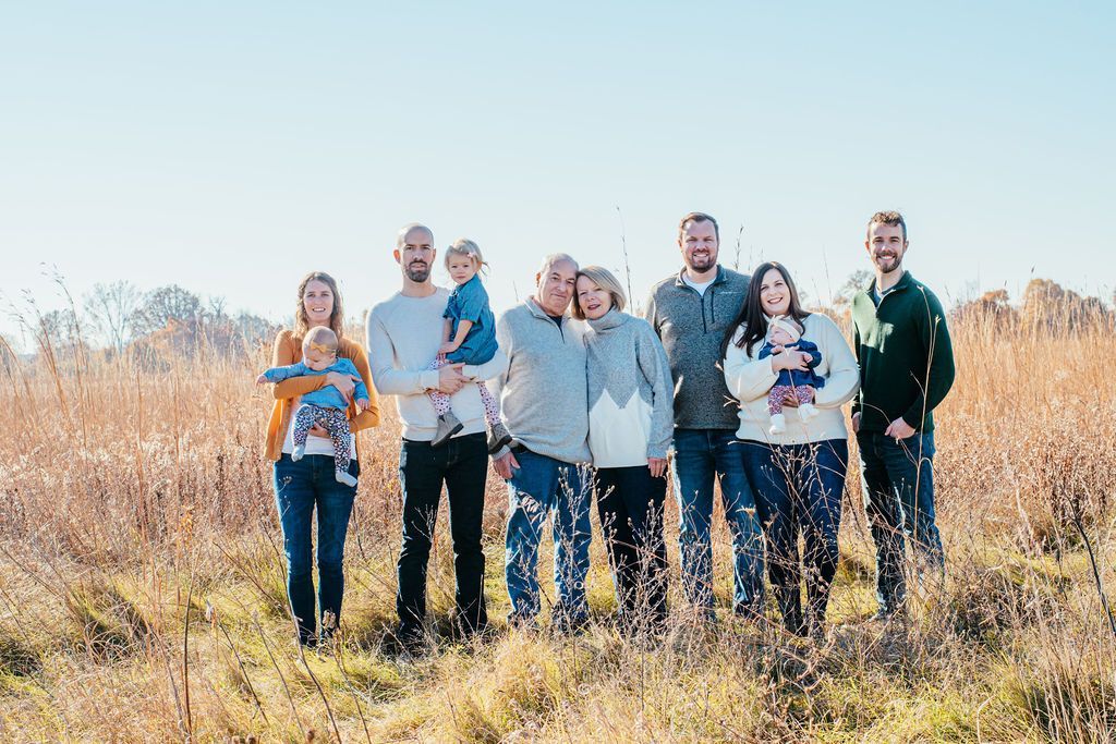Seven people standing together in a grassy field on a sunny day, smiling at the camera.