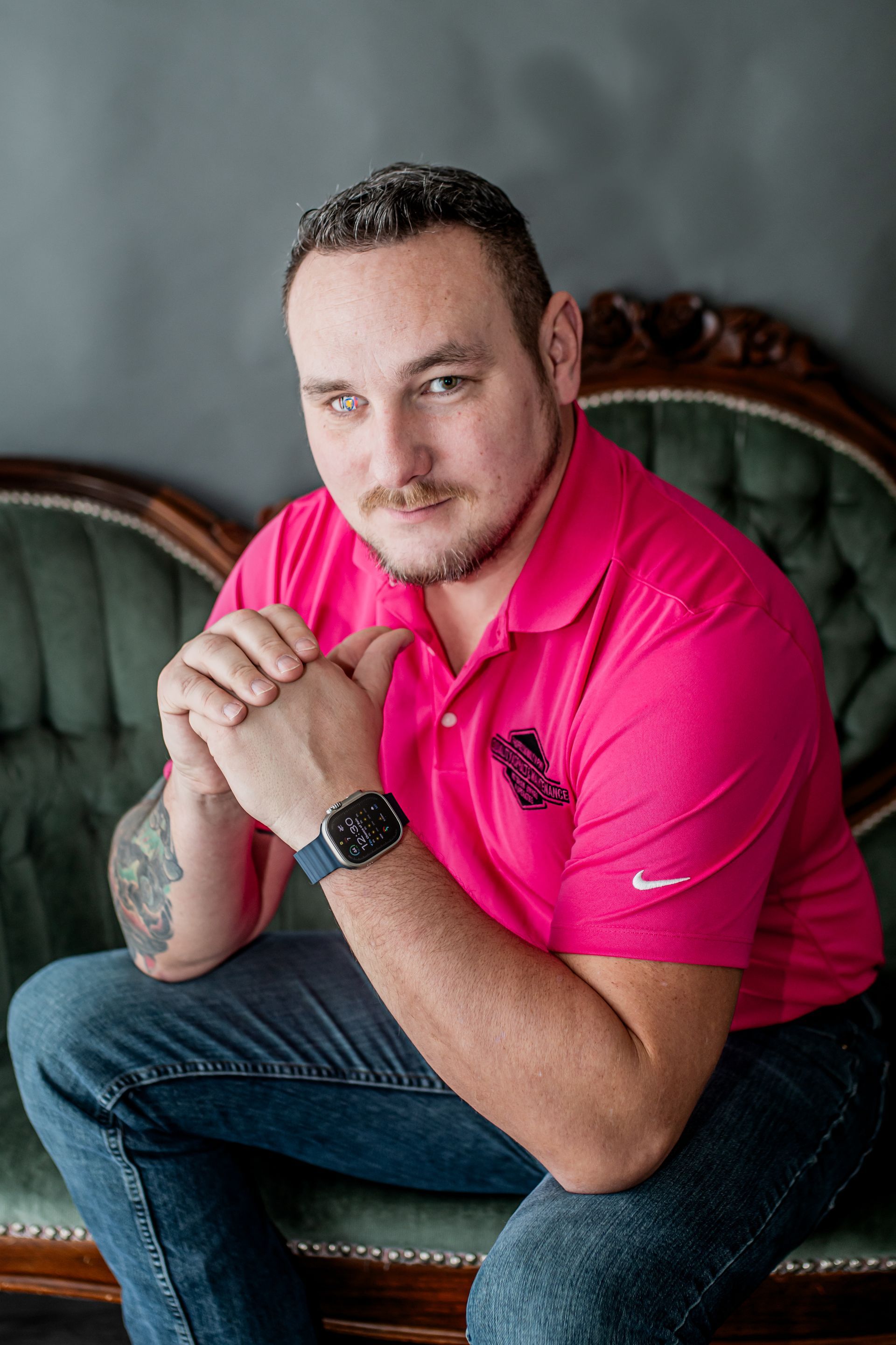 Person in a bright pink shirt sitting on a chair, leaning forward with hands clasped.
