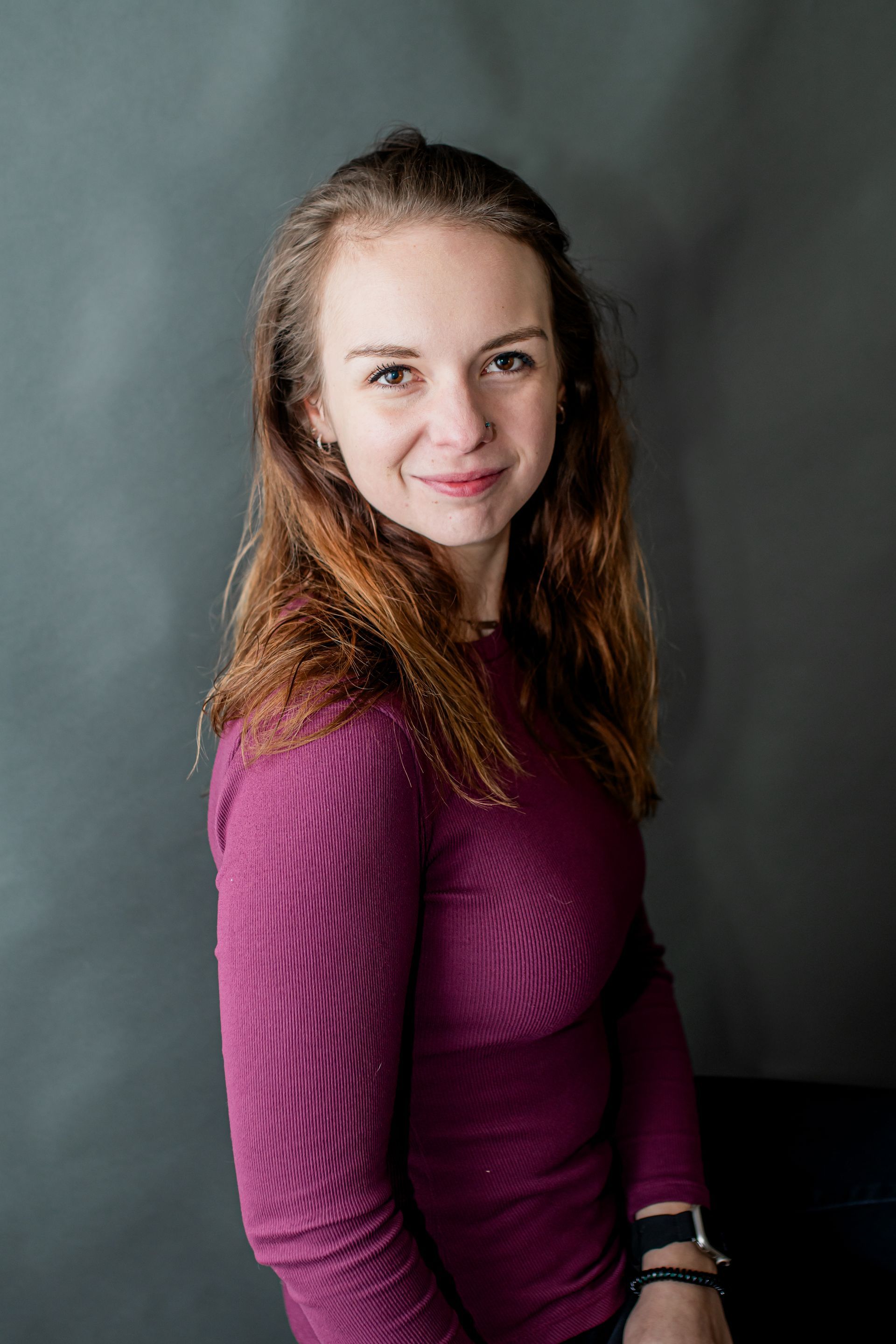 Portrait of a woman in a magenta sweater, smiling against a dark gray backdrop.