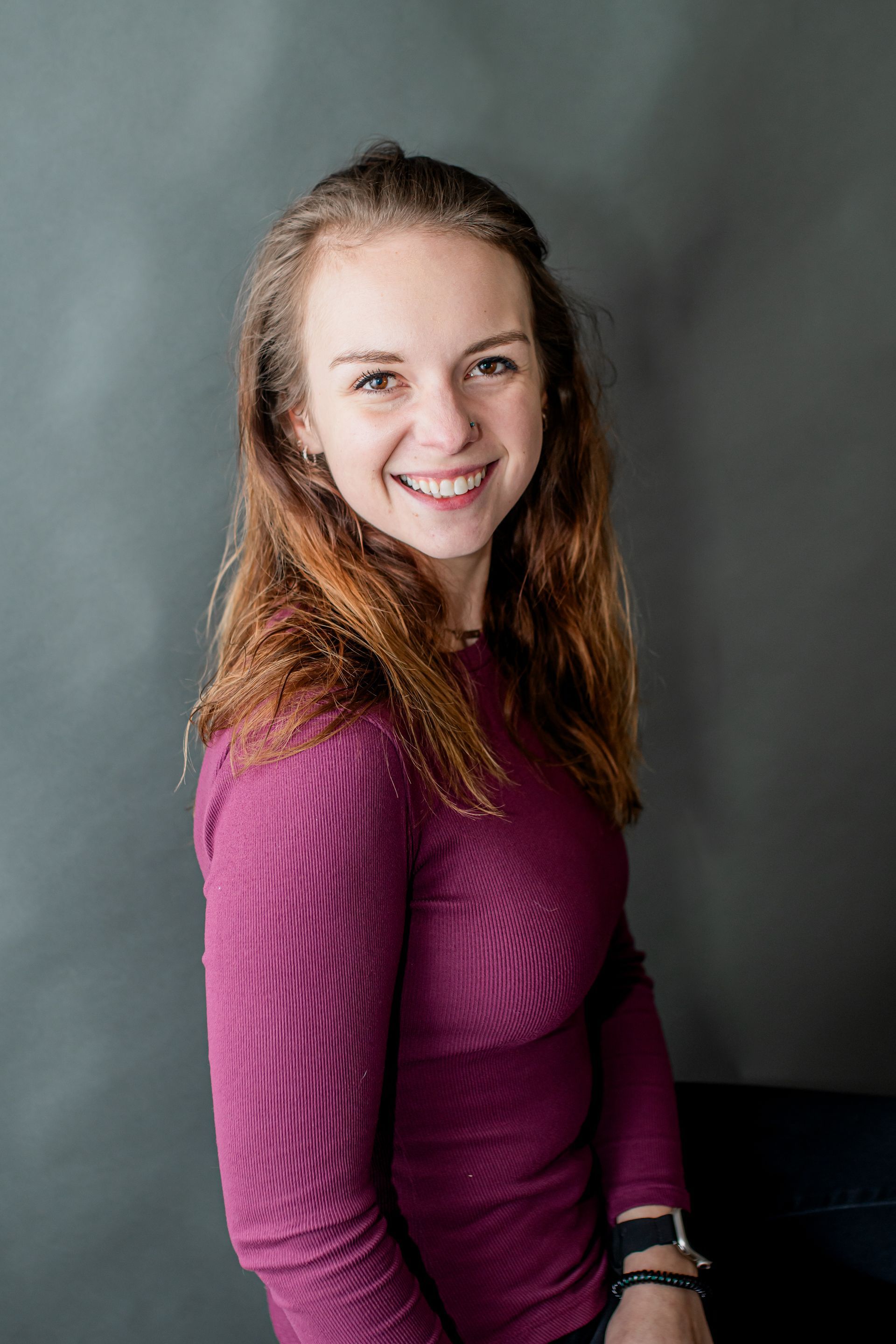 Smiling woman in a magenta sweater seated against a gray backdrop