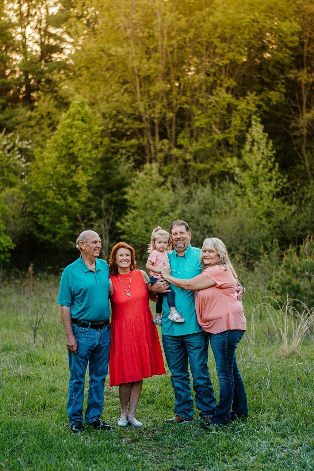 Five people posing outdoors in a grassy field, with trees and warm sunlight in the background.