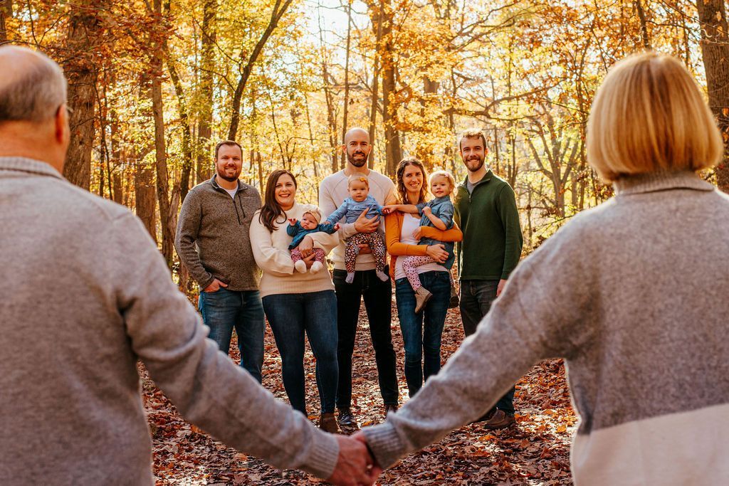 People holding hands in a forest during autumn, smiling and gathered in a circle.