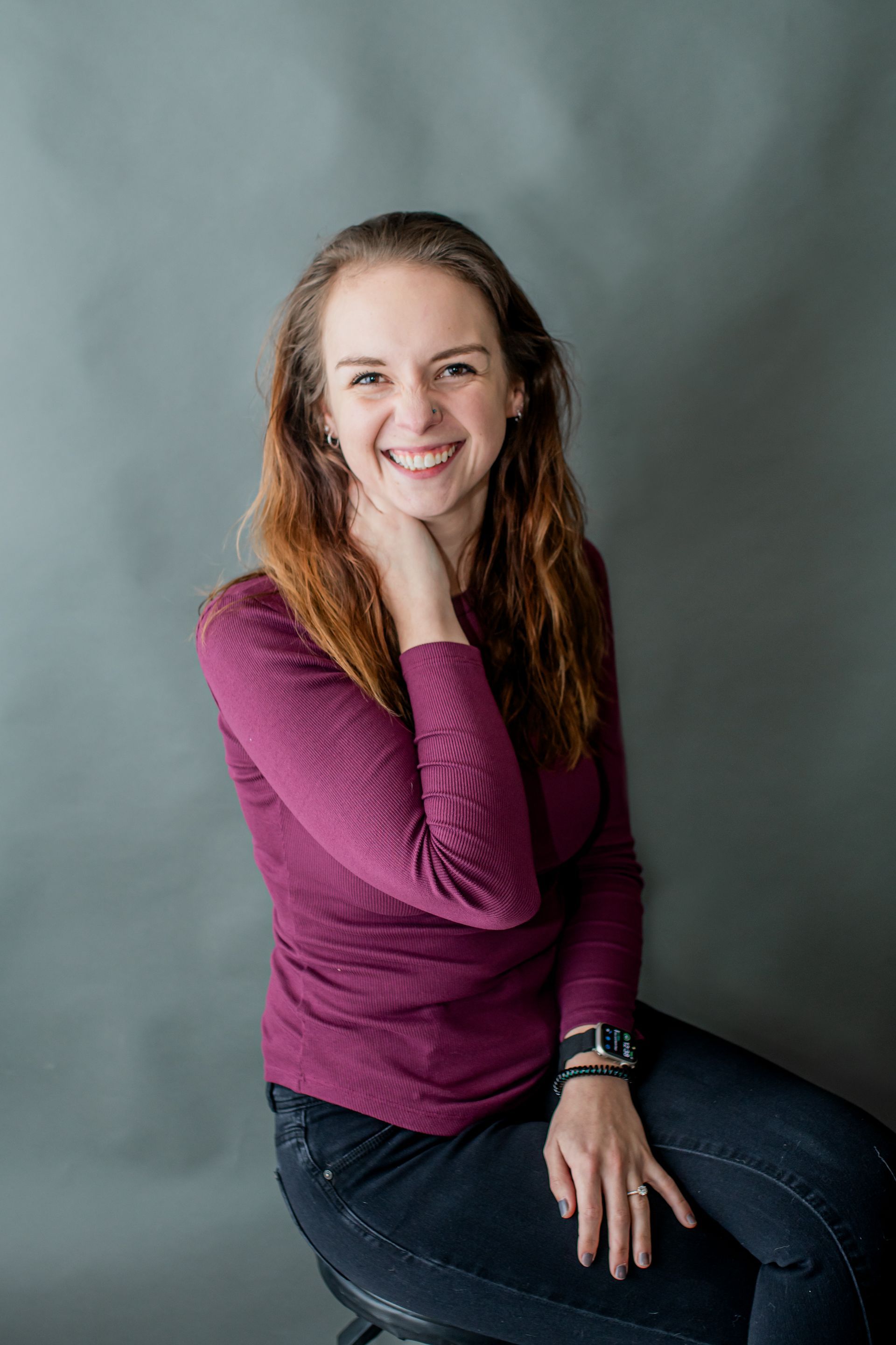Smiling woman in a purple top seated against a gray studio backdrop