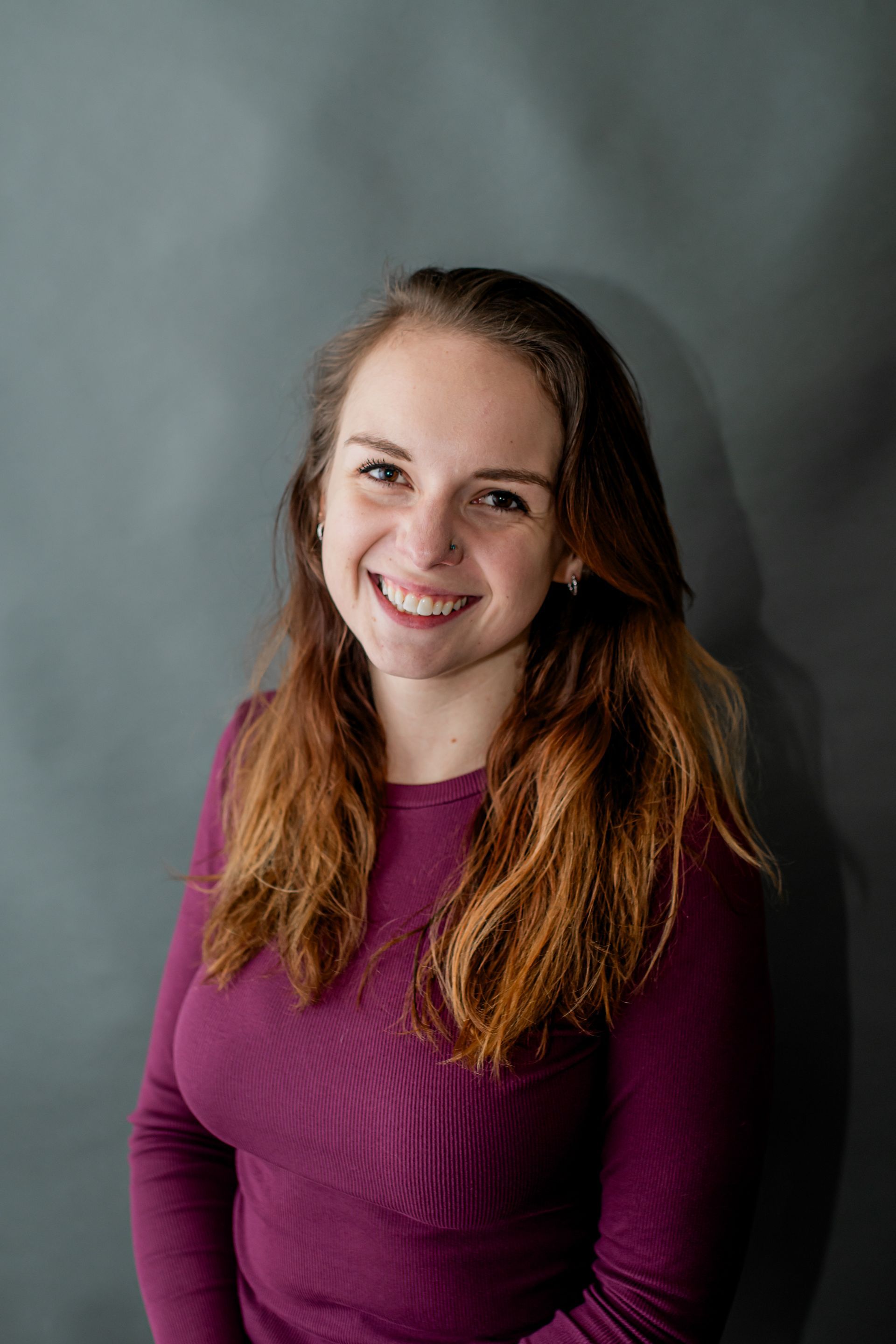 Smiling person in a purple sweater against a gray studio background