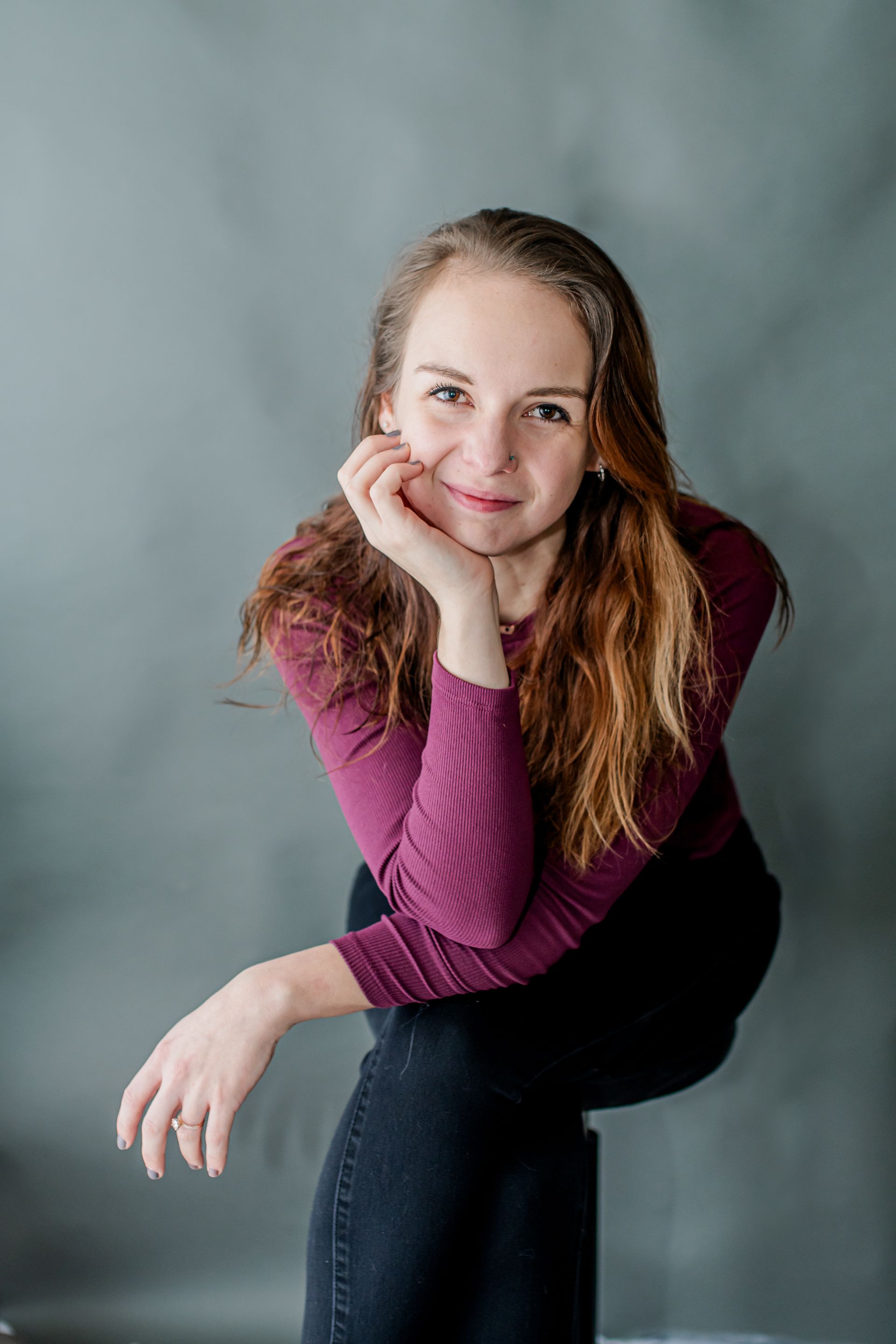 Person crouching and smiling in a magenta sweater against a gray studio backdrop