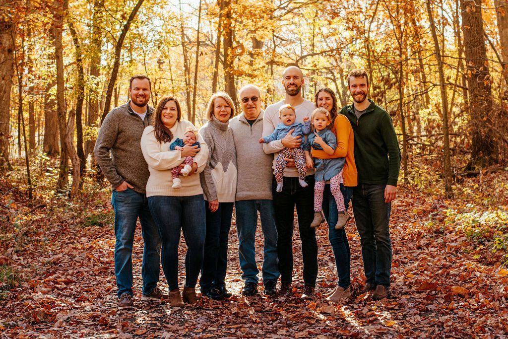 Group of seven people standing together in a sunlit autumn forest with fallen orange leaves