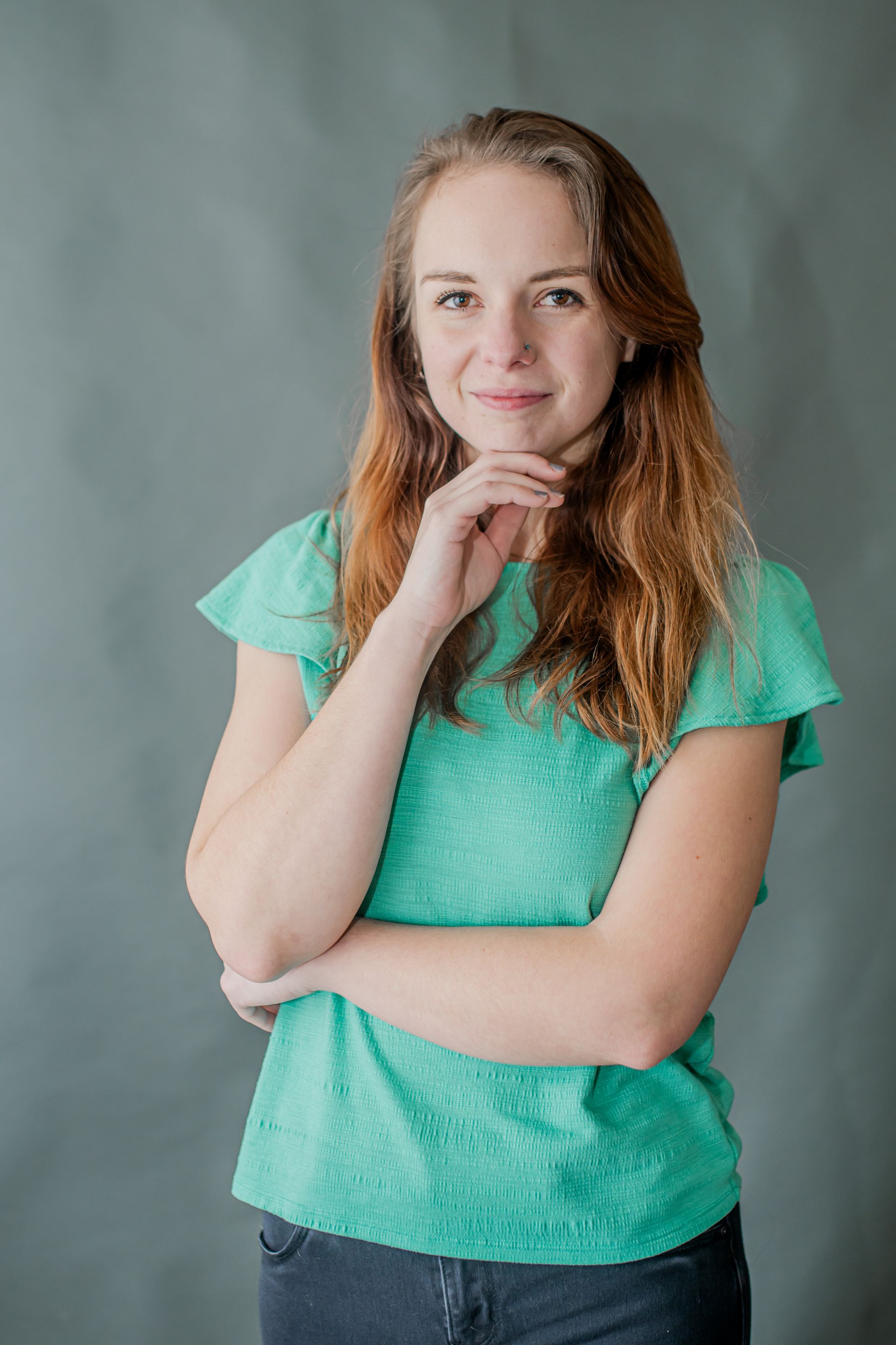Woman in a turquoise shirt posing thoughtfully against a gray backdrop