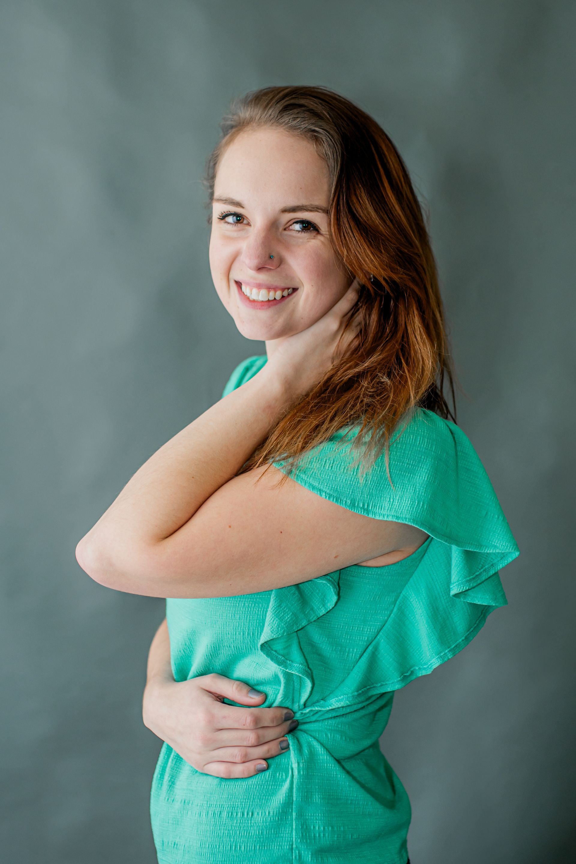Smiling woman in a teal dress posing against a gray studio backdrop