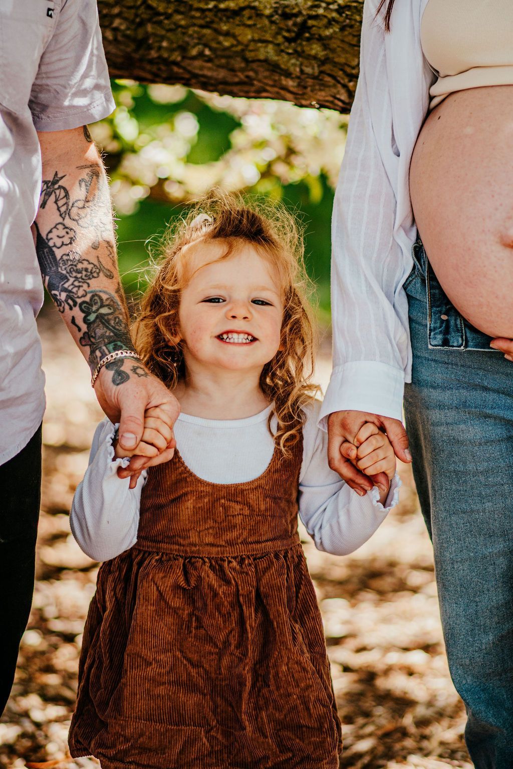 Smiling child holding hands with two adults outdoors on a sunny day