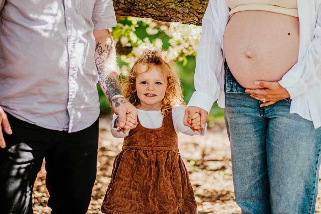 Family holding hands with a smiling child outdoors in a sunlit park