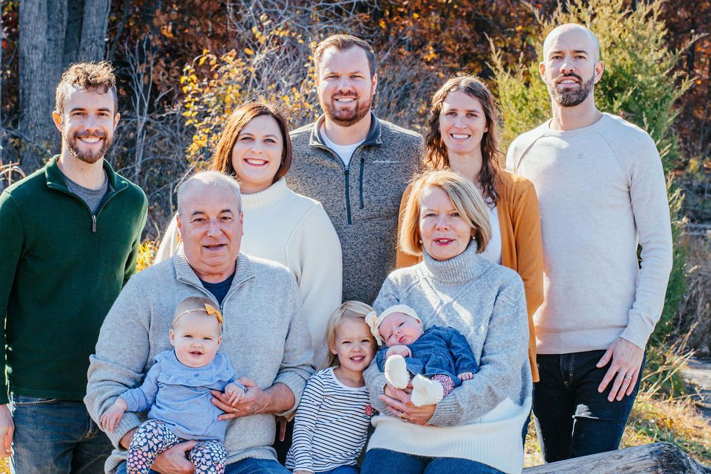 Group of people posing outdoors in a family portrait, smiling in warm sunlight.