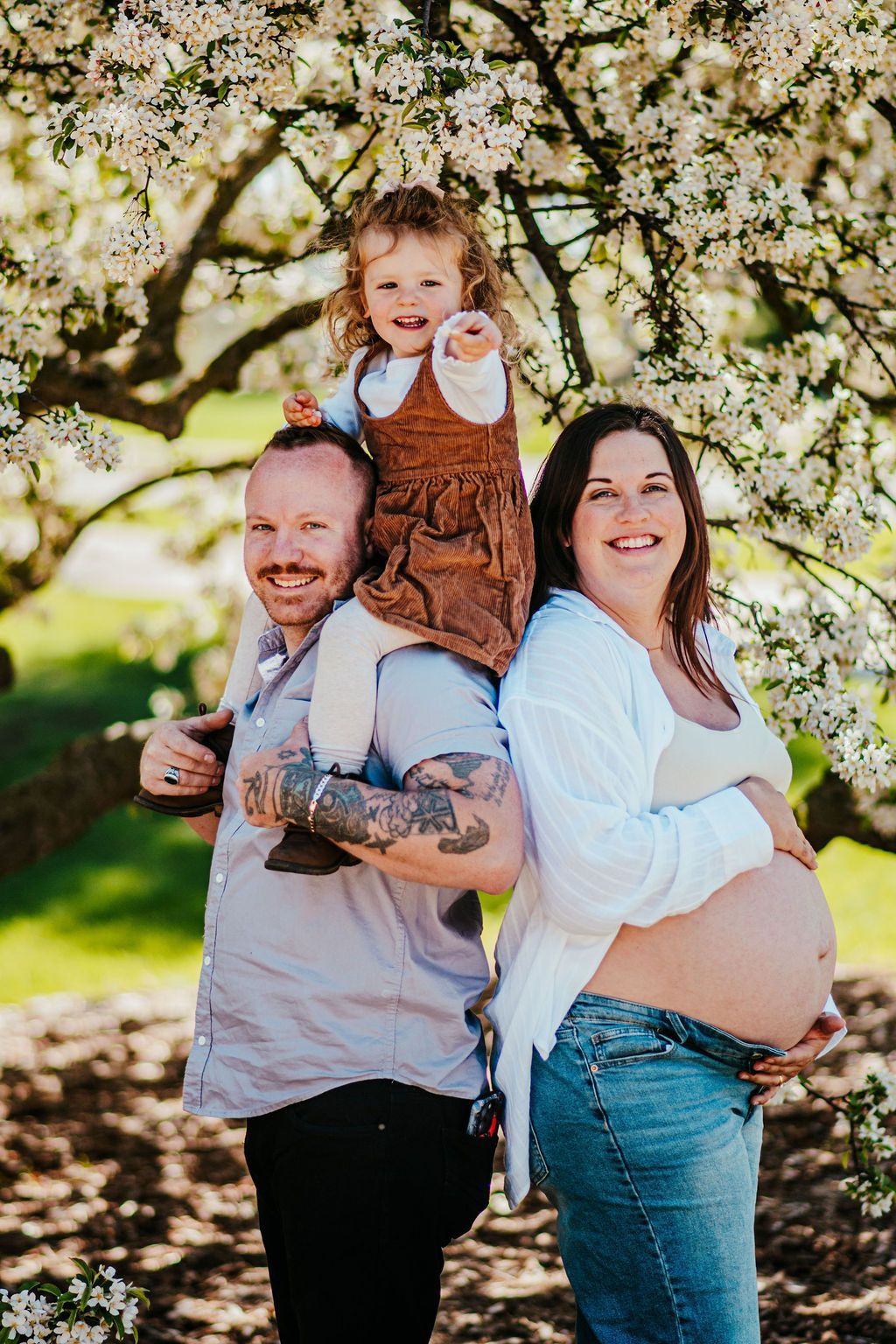 Smiling family with child in a blossoming orchard, standing together outdoors in sunlight.