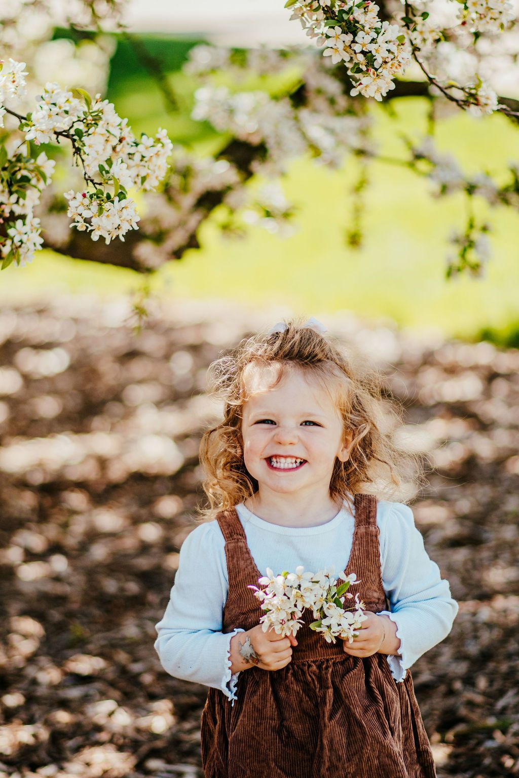 Smiling child holding flowers under blooming tree branches in a sunlit garden