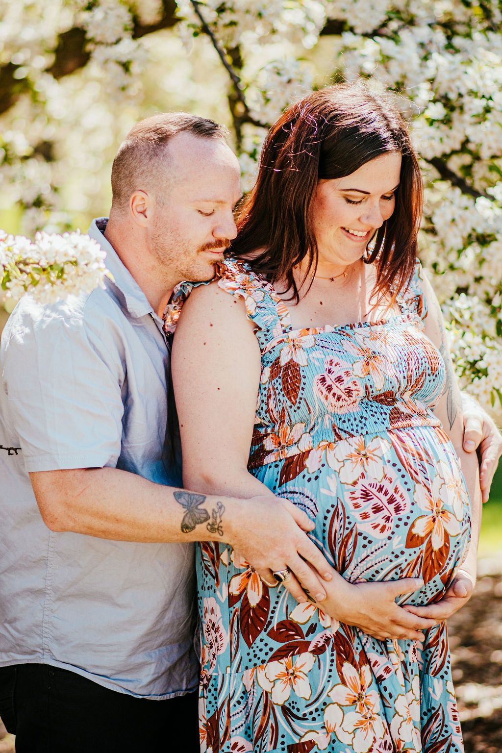 Pregnant couple embracing outdoors among blooming white flowers
