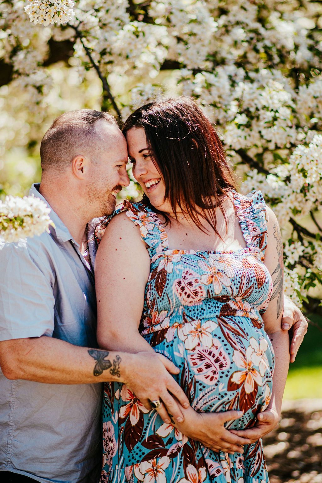 Couple embracing outdoors beneath blooming white flowers, smiling close together