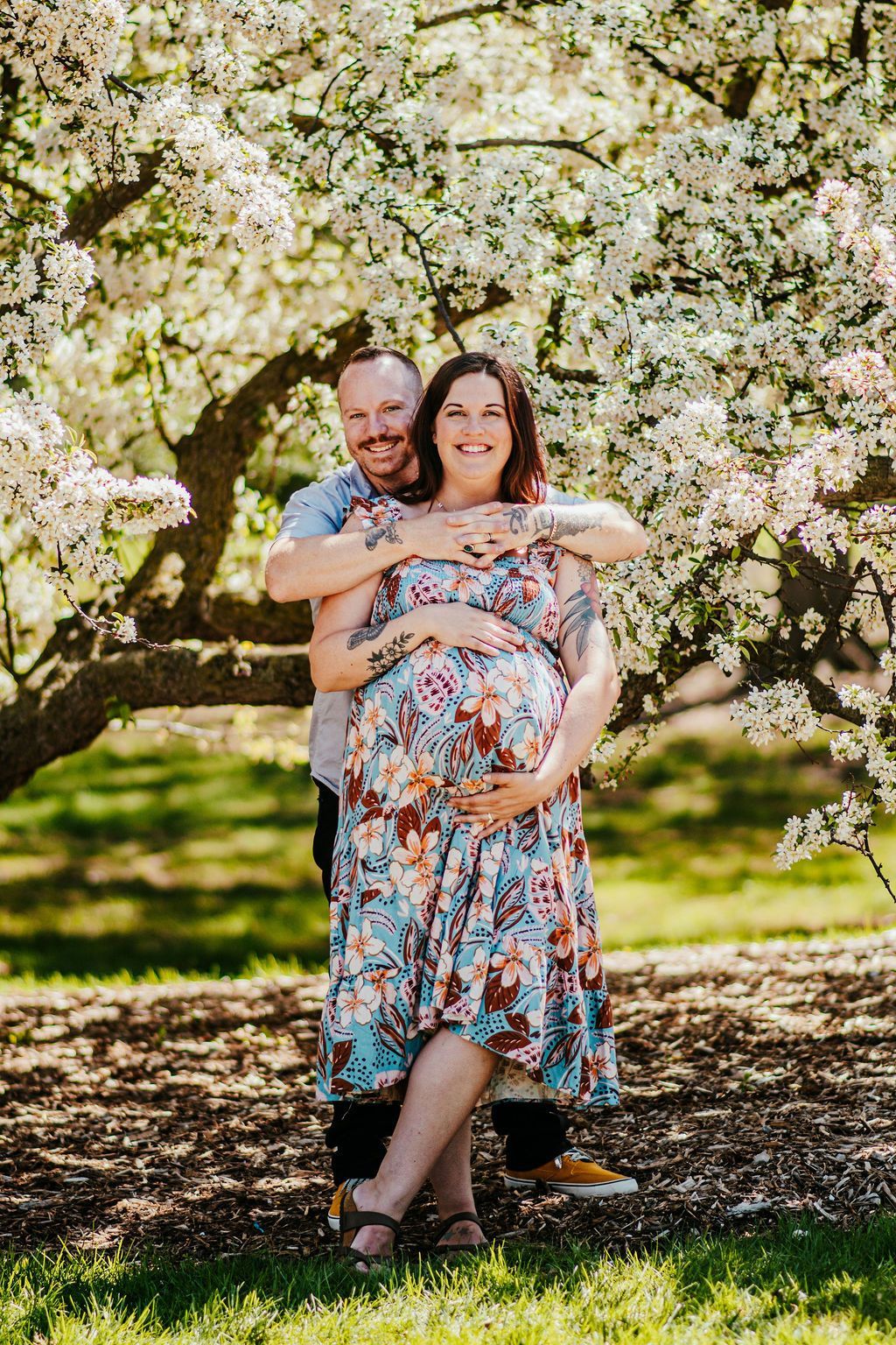 Pregnant woman and man hugging under a blooming tree in a sunny orchard