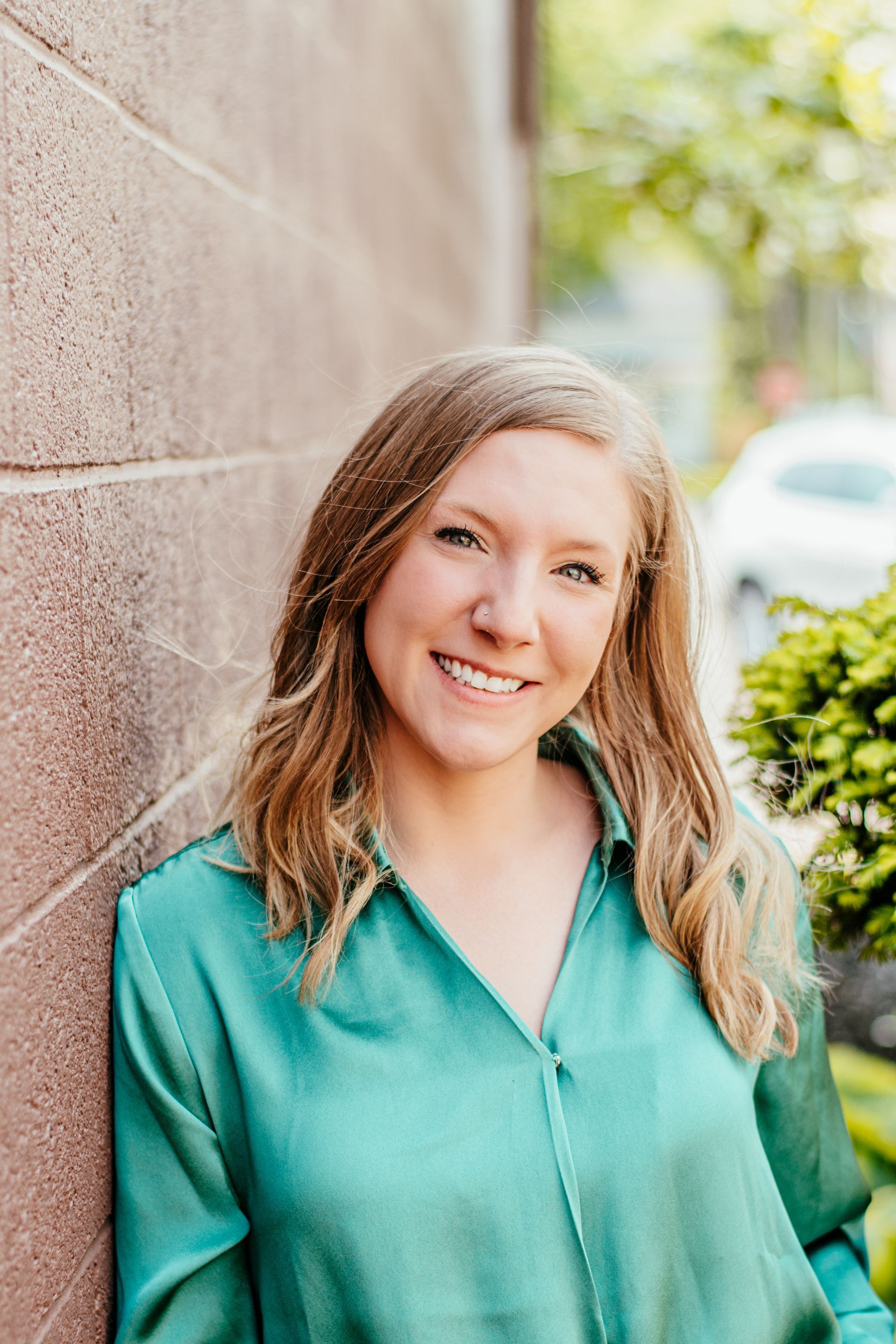 Smiling woman in a green blouse leaning against a brick wall outdoors