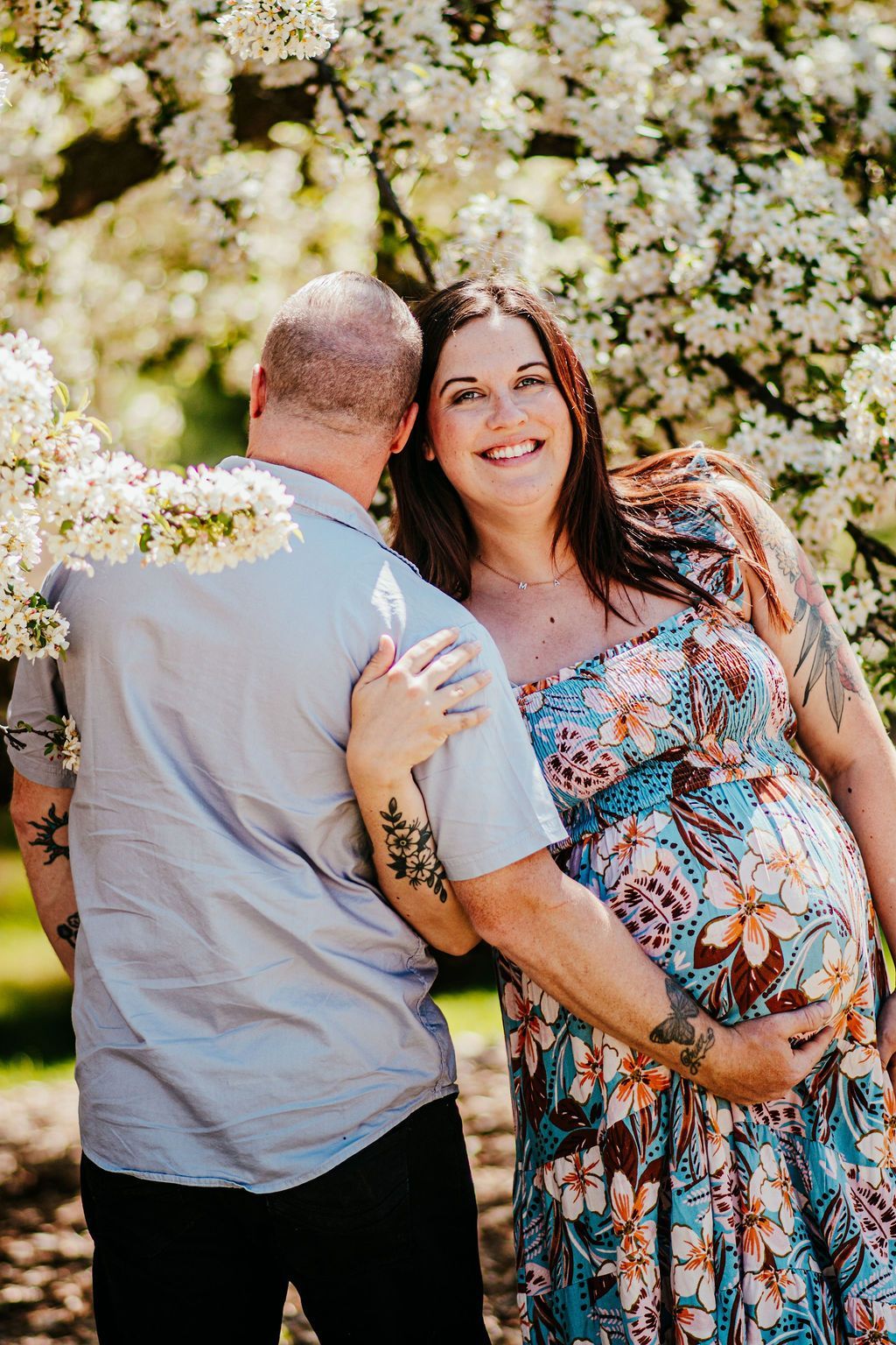 Couple standing among blooming white flowers, smiling and embracing outdoors.