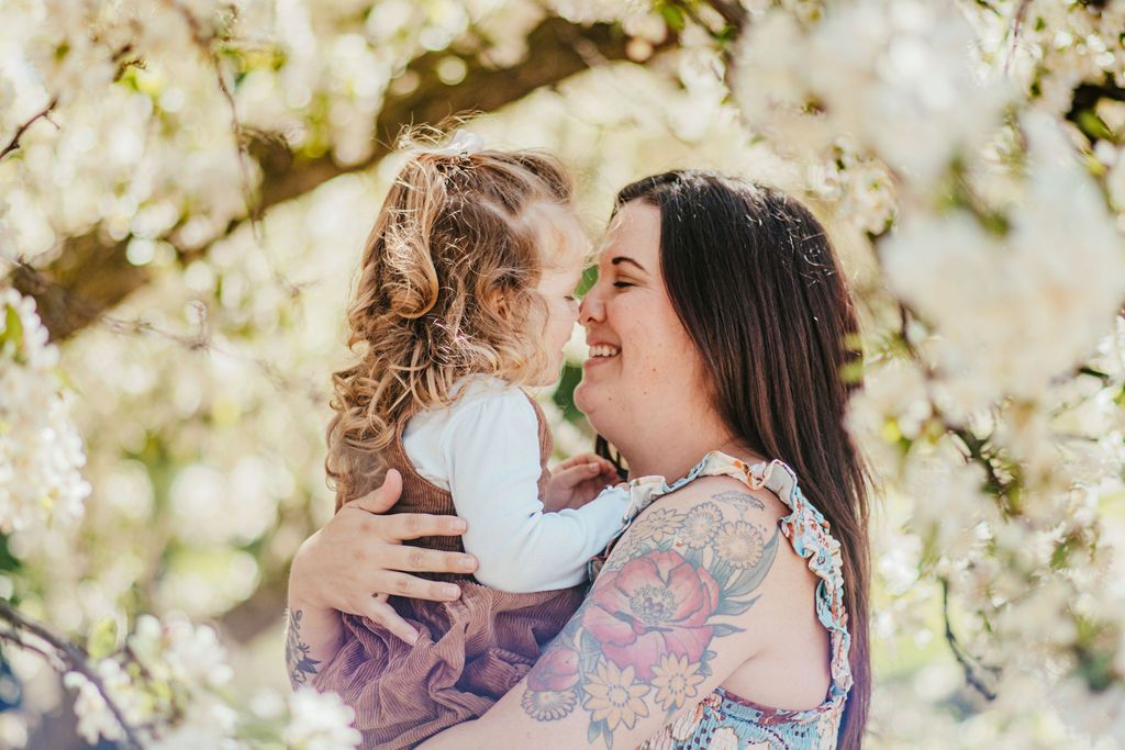 Woman holding a smiling child outdoors among blooming white flowers