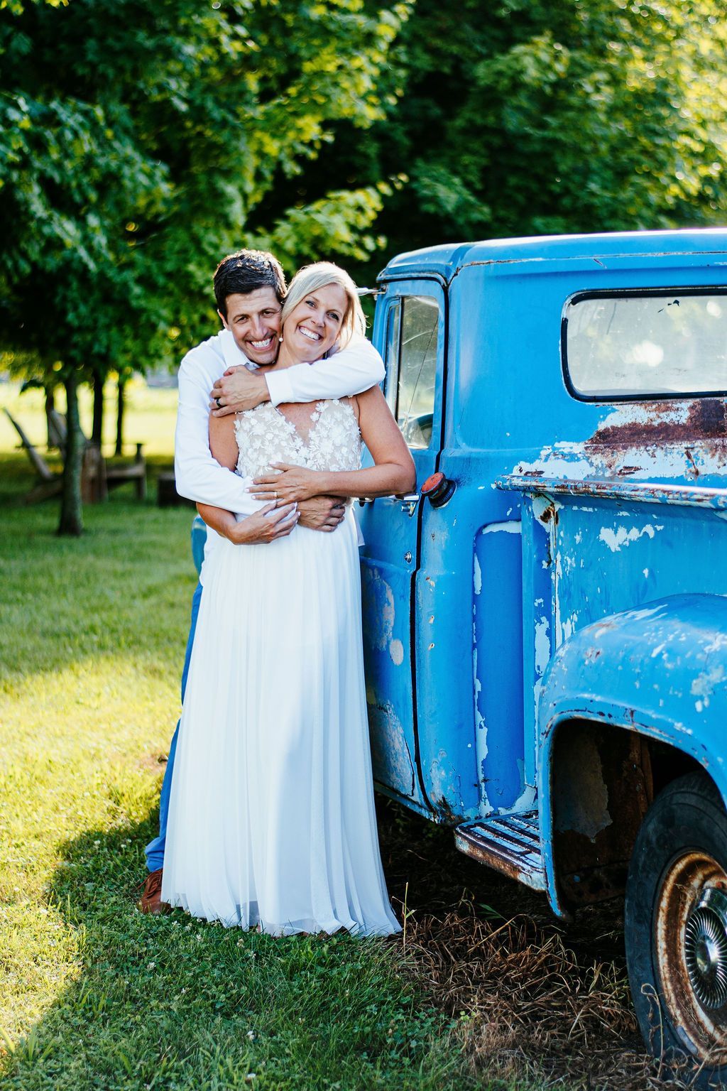 Couple embracing beside a blue vintage truck in a sunny grassy yard