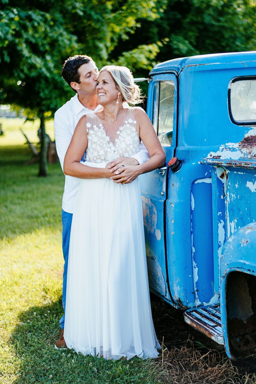 Couple embracing beside a blue vintage truck in a sunny outdoor setting