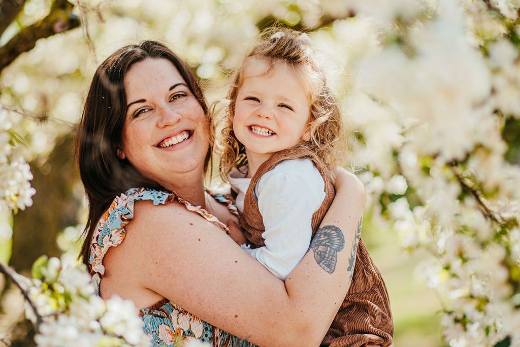Woman hugging a smiling child outdoors, both in bright sunlight with blurred greenery behind them