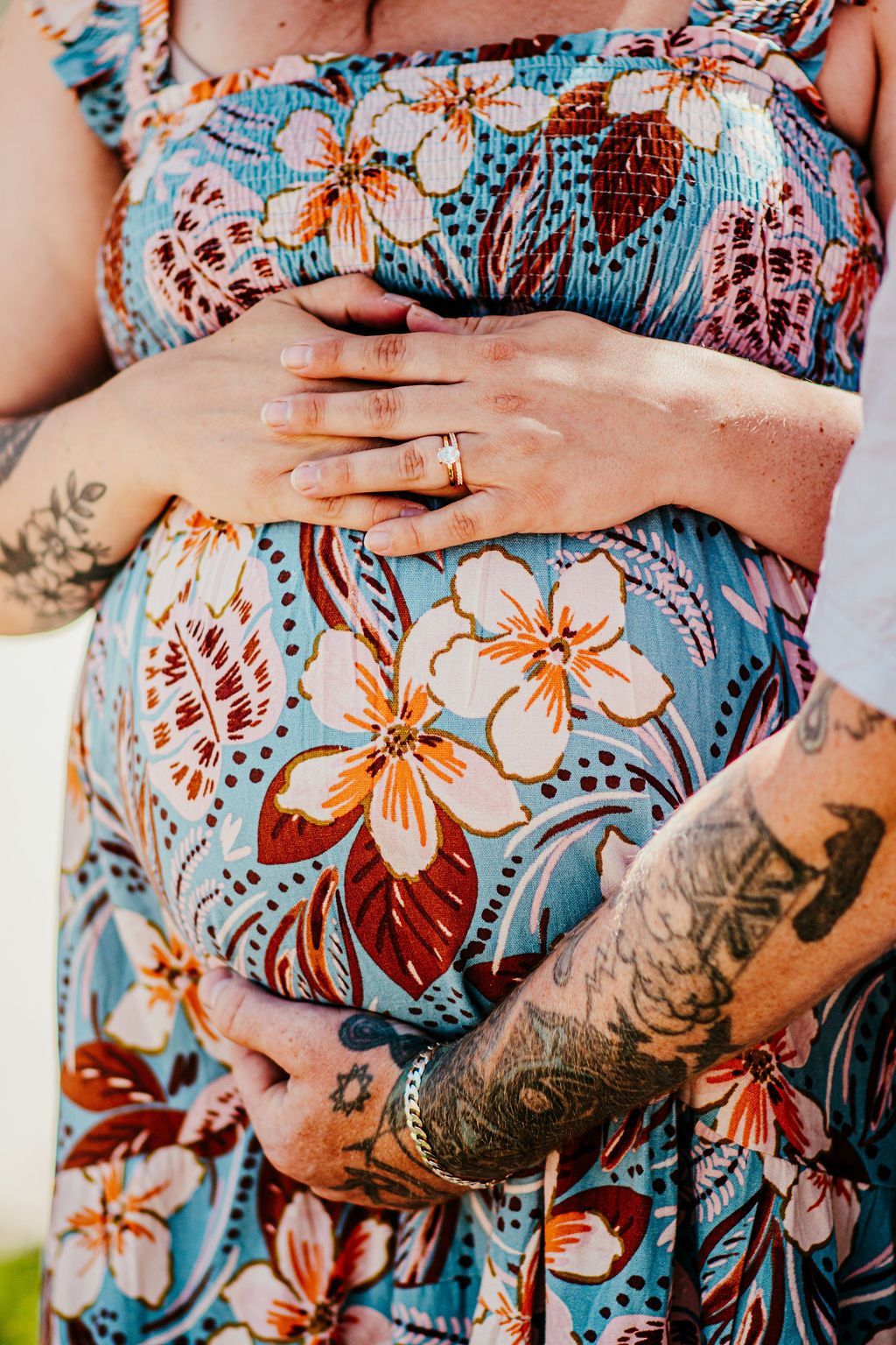 Close-up of hands resting on a pregnant belly, with floral tattoos and a colorful patterned dress