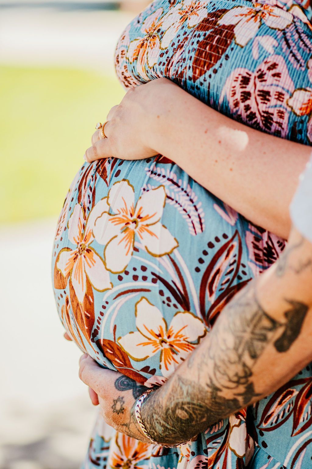 Two hands cradling a pregnant belly in a floral dress