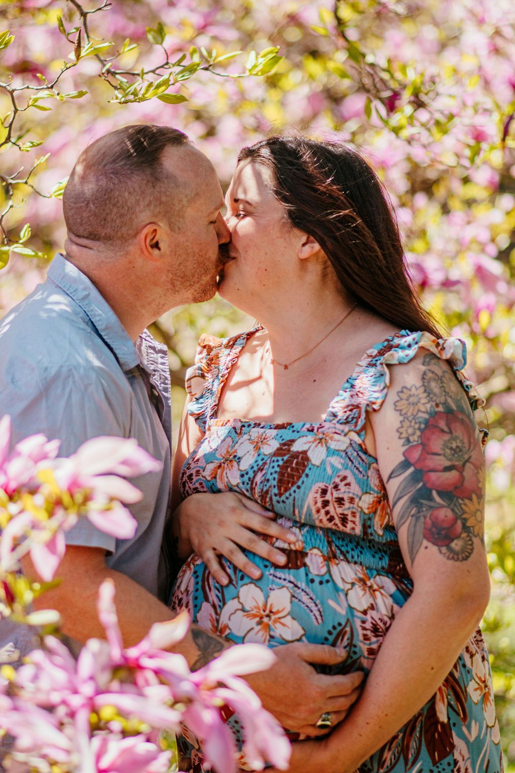 Couple kissing in a flowering garden, with the woman holding her pregnant belly.